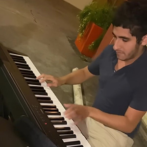 Performer Sal Martinez sitting at a piano outdoors
